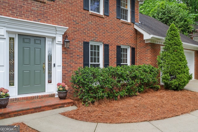 entrance to property with brick siding, roof with shingles, a garage, and concrete driveway