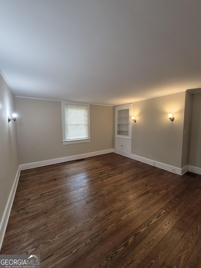 unfurnished room with dark wood finished floors, built in features, baseboards, and crown molding