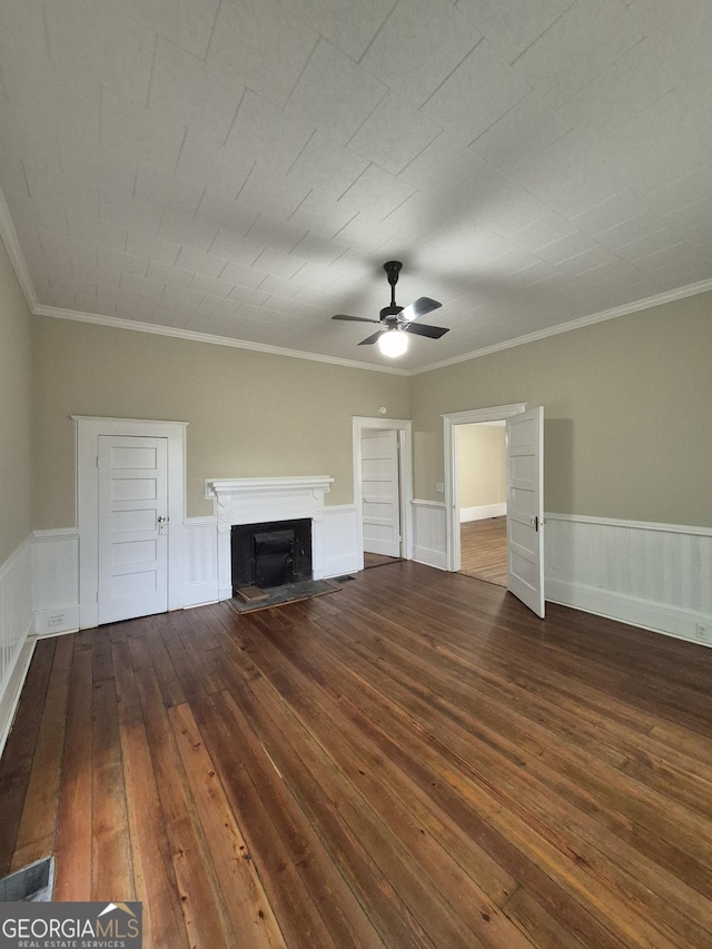 unfurnished living room with wood-type flooring, a ceiling fan, a fireplace, wainscoting, and ornamental molding