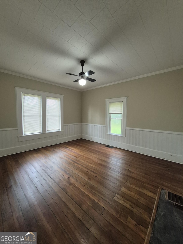 unfurnished room featuring crown molding, dark wood-style flooring, wainscoting, and ceiling fan