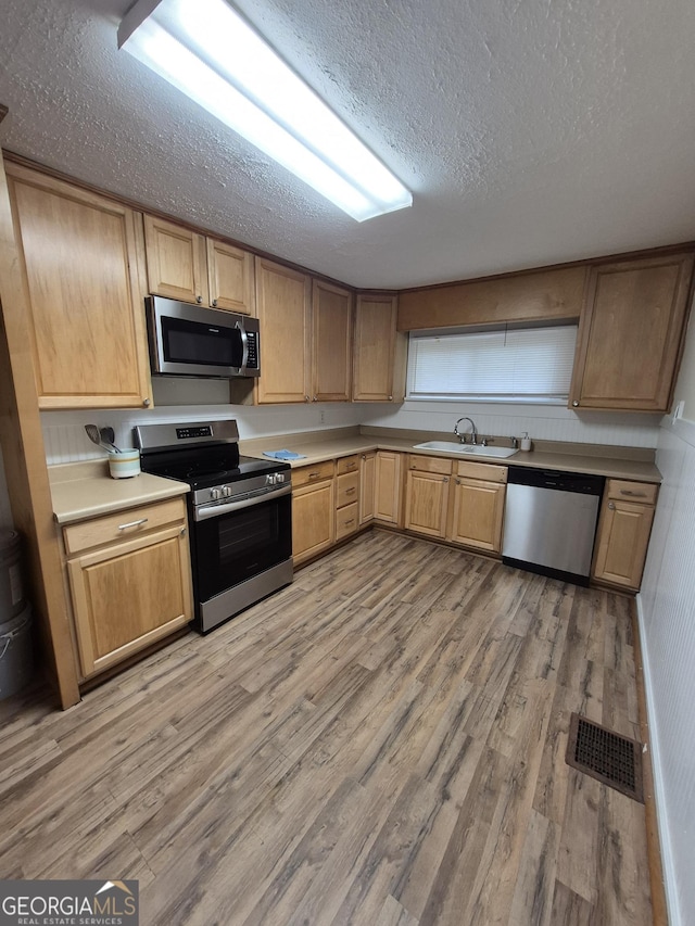 kitchen featuring stainless steel appliances, a textured ceiling, a sink, light wood-style flooring, and light countertops