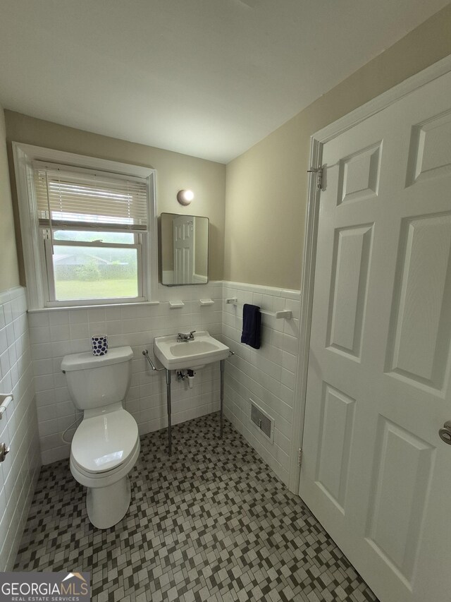 half bathroom featuring tile walls, wainscoting, and toilet