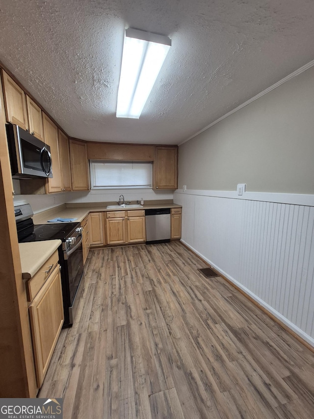 kitchen with appliances with stainless steel finishes, light wood-style floors, a textured ceiling, a sink, and light countertops