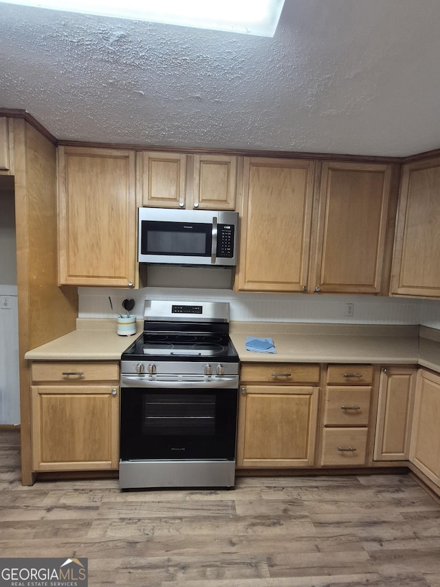 kitchen with appliances with stainless steel finishes, light countertops, a textured ceiling, light wood-style floors, and light brown cabinetry