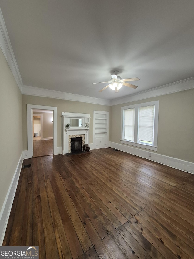 unfurnished living room featuring ceiling fan, dark wood-type flooring, ornamental molding, a stone fireplace, and baseboards