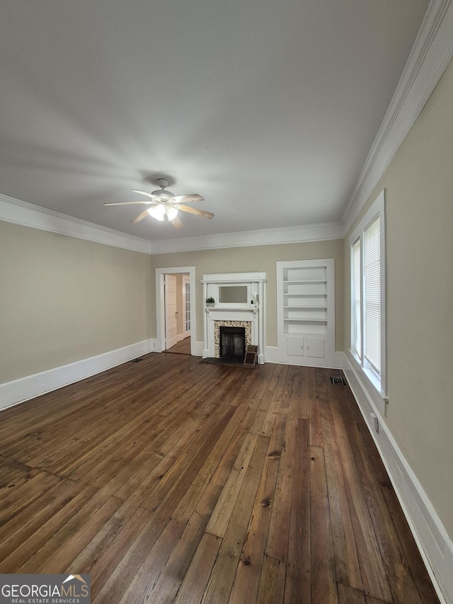 unfurnished living room with dark wood-type flooring, built in features, a brick fireplace, ceiling fan, and crown molding