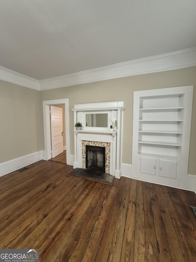 unfurnished living room with ornamental molding, hardwood / wood-style flooring, built in features, a stone fireplace, and baseboards