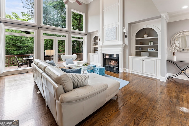 living room with ornamental molding, a towering ceiling, a fireplace with flush hearth, plenty of natural light, and built in shelves