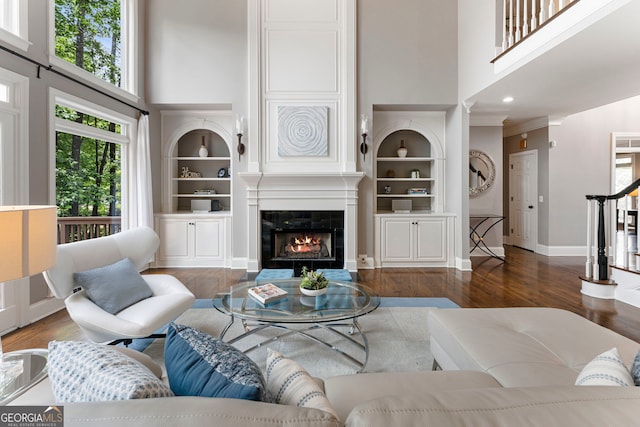 living area featuring a towering ceiling, a large fireplace, wood finished floors, built in features, and baseboards
