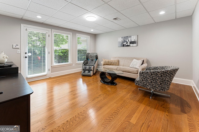 living room featuring a paneled ceiling, baseboards, and wood finished floors