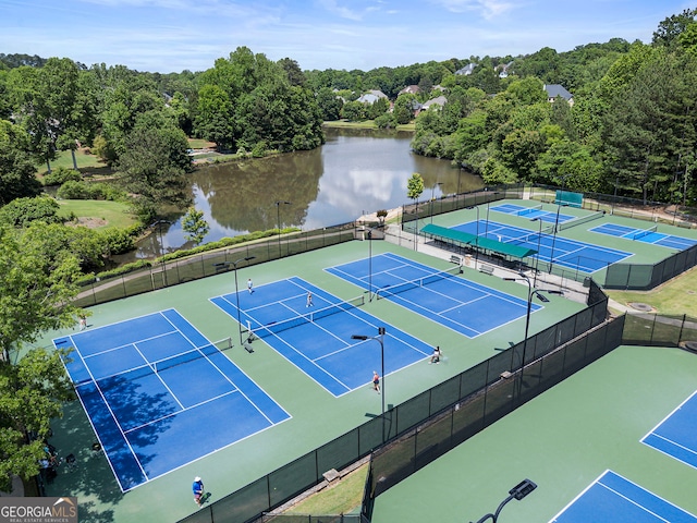 view of tennis court with a water view and fence