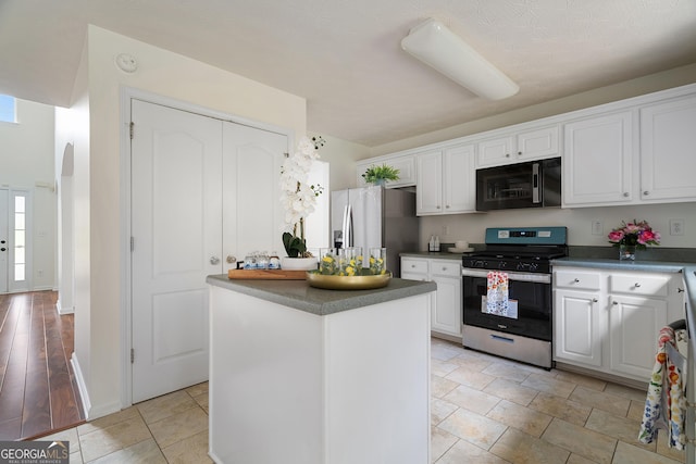 kitchen featuring stainless steel appliances, white cabinets, a kitchen island, dark countertops, and baseboards