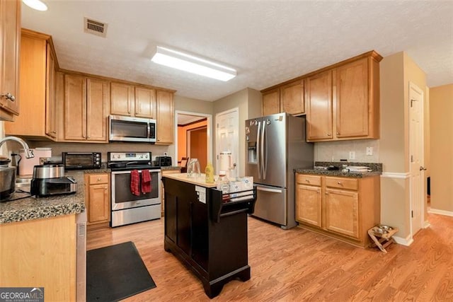 3265 Watson Gate Rd, Loganville, GA 30052 - kitchen featuring stainless steel appliances, light wood-style floors, a center island, dark countertops, and baseboards