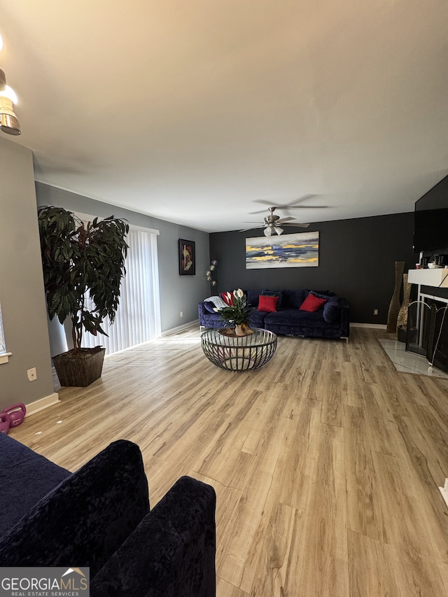 living room featuring wood finished floors, a ceiling fan, baseboards, and a fireplace with flush hearth