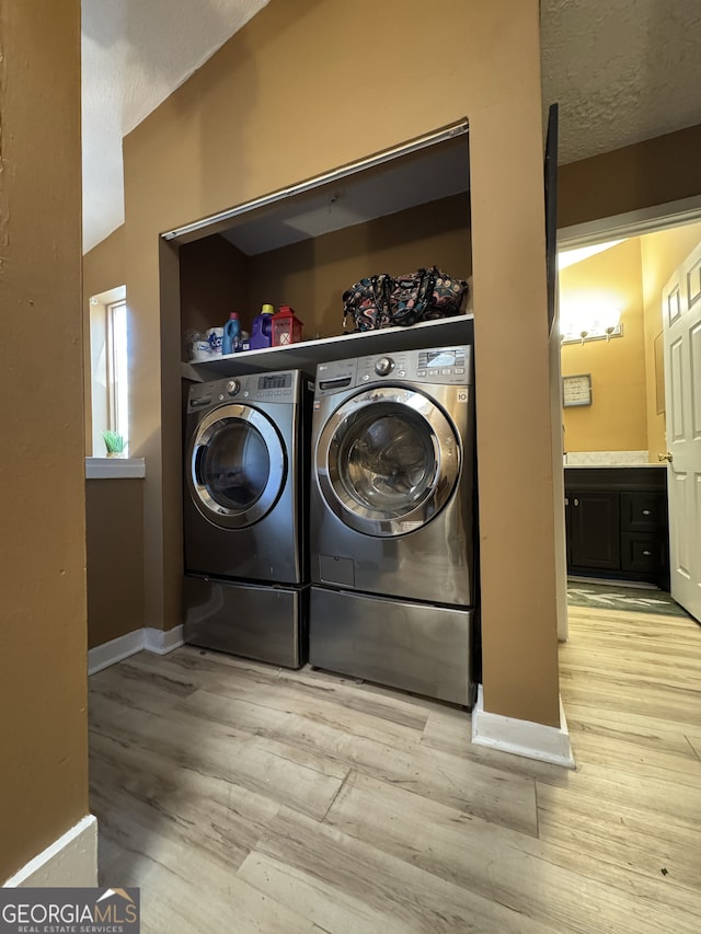 laundry room featuring light wood-type flooring, independent washer and dryer, baseboards, and a textured ceiling