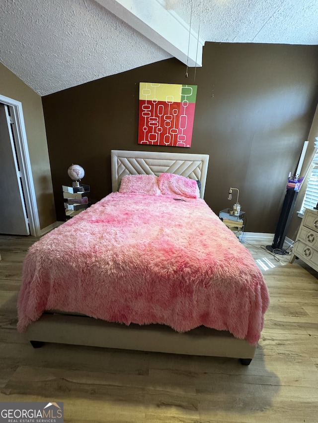 bedroom with wood finished floors, a textured ceiling, vaulted ceiling, and baseboards