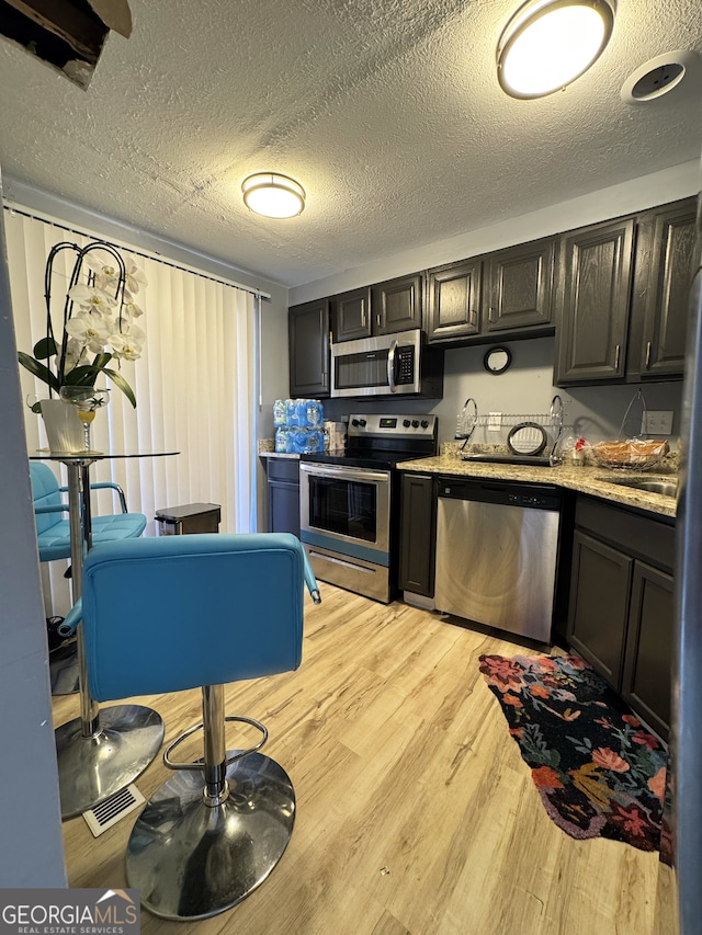 kitchen featuring appliances with stainless steel finishes, light wood-type flooring, a textured ceiling, and light stone counters