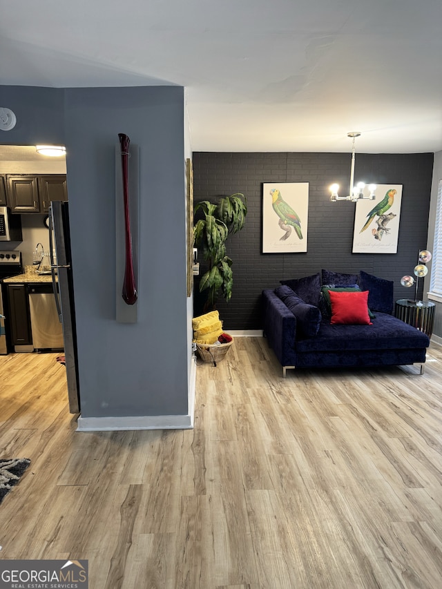 living area featuring light wood-style flooring, a chandelier, and brick wall