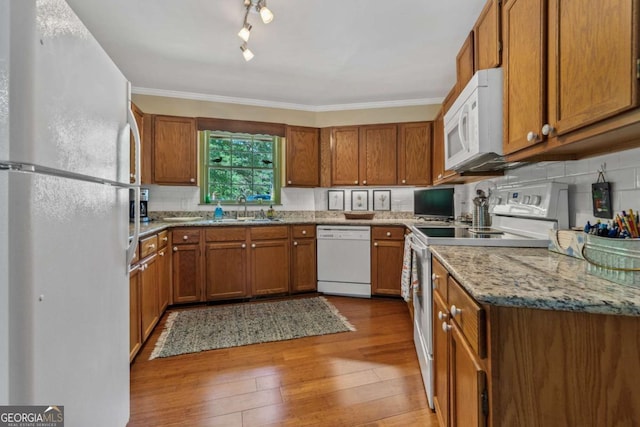 kitchen with white appliances, a sink, brown cabinetry, and crown molding