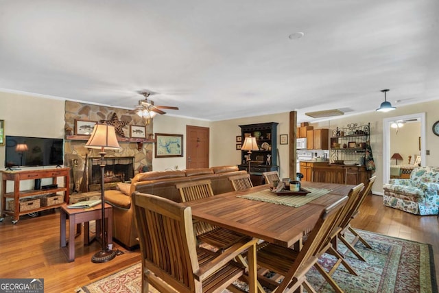 dining space with a ceiling fan, light wood finished floors, a fireplace, and crown molding