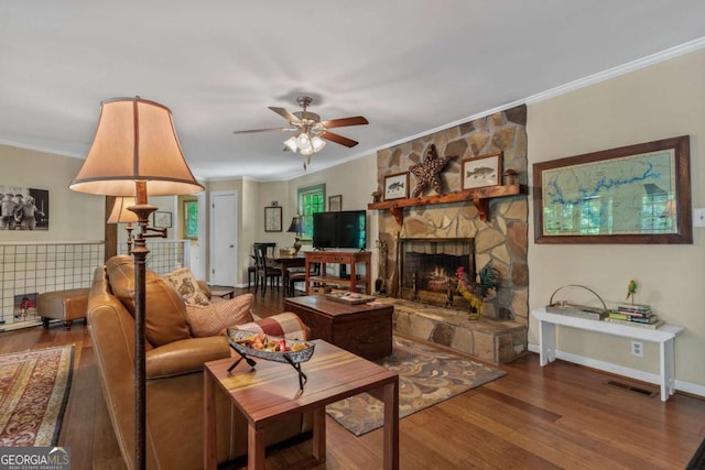 living area featuring wood finished floors, ornamental molding, a ceiling fan, and a stone fireplace