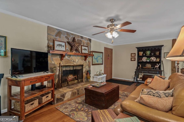 living room with a ceiling fan, wood finished floors, a fireplace, crown molding, and baseboards