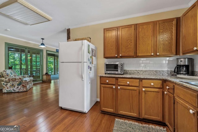 kitchen with freestanding refrigerator, brown cabinets, crown molding, decorative backsplash, and dark wood finished floors