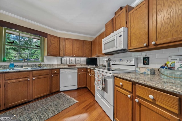 kitchen featuring white appliances, a sink, brown cabinetry, crown molding, and tasteful backsplash