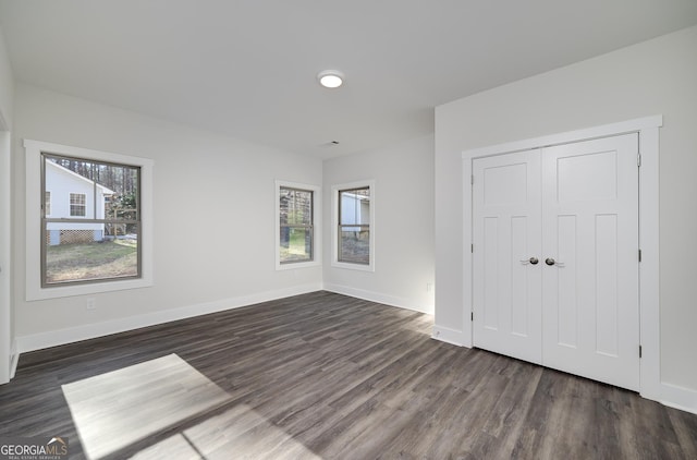 unfurnished bedroom featuring dark wood-style floors, baseboards, and a closet