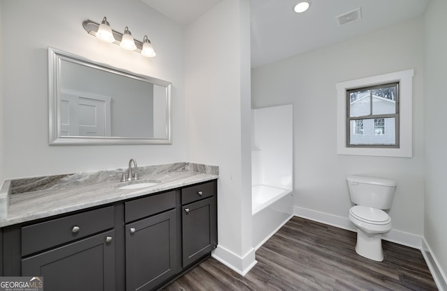 bathroom with baseboards, toilet, wood finished floors, vanity, and a tub