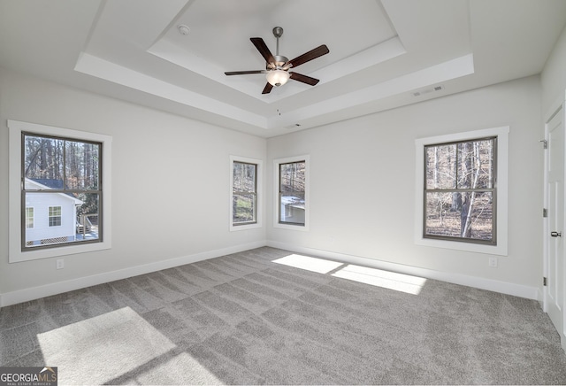 carpeted spare room featuring a tray ceiling, plenty of natural light, a ceiling fan, and baseboards