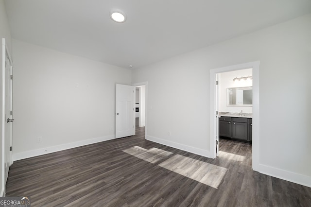 unfurnished bedroom with dark wood finished floors, baseboards, a sink, and ensuite bathroom