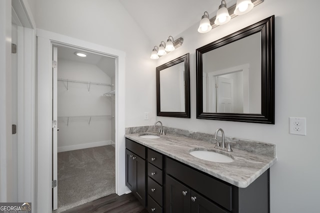 bathroom featuring lofted ceiling, double vanity, a spacious closet, baseboards, and wood finished floors