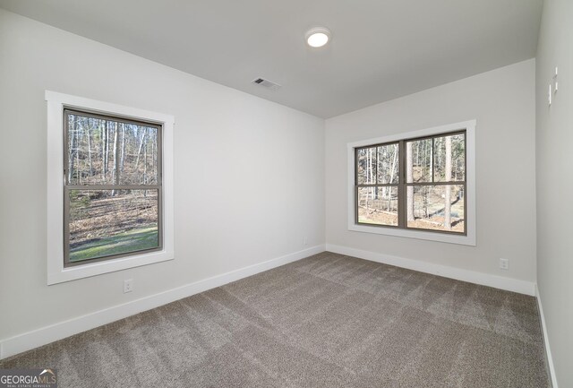 spare room with dark carpet, plenty of natural light, and baseboards