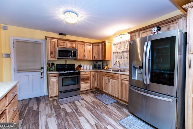 kitchen with appliances with stainless steel finishes, a sink, light countertops, and dark wood-type flooring