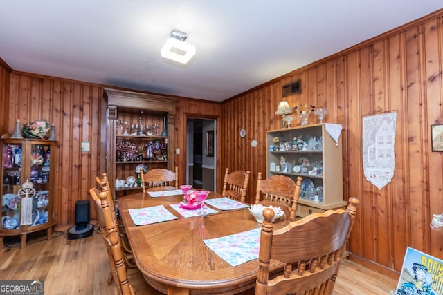 dining space with wooden walls, light wood finished floors, and crown molding