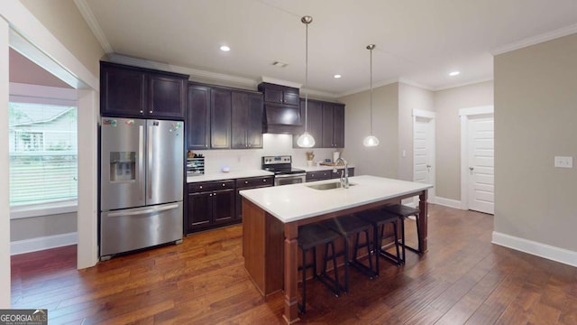 kitchen with stainless steel appliances, a sink, crown molding, a center island with sink, and baseboards
