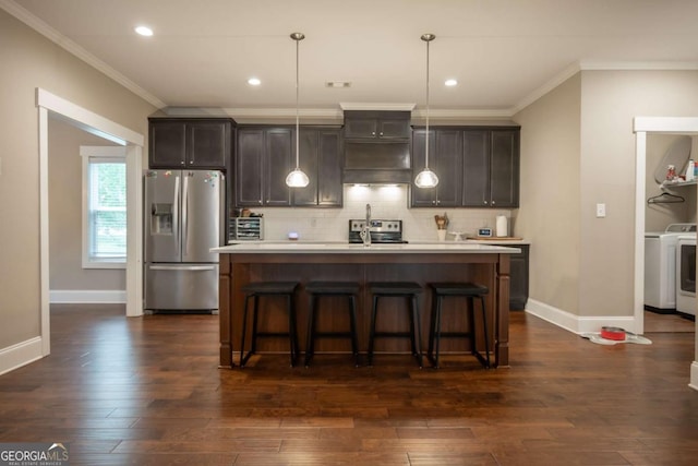 kitchen with appliances with stainless steel finishes, ornamental molding, light countertops, washer / clothes dryer, and a kitchen island with sink