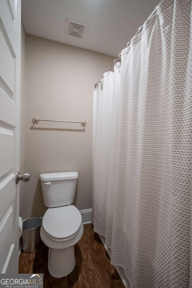bathroom with wood finished floors, toilet, baseboards, and a shower with shower curtain