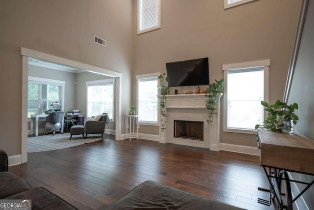 living room with a towering ceiling, wood finished floors, baseboards, and a fireplace with flush hearth