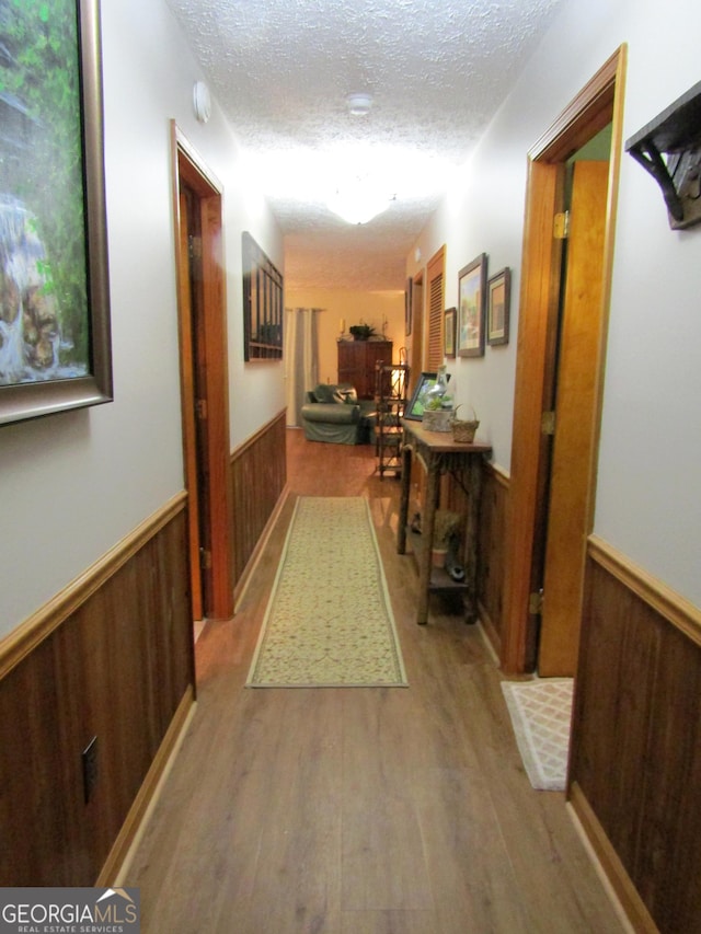 hall with a wainscoted wall, wooden walls, a textured ceiling, and wood finished floors
