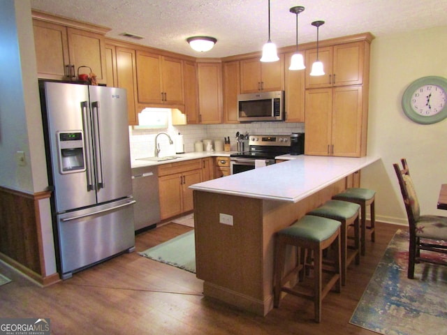 kitchen featuring appliances with stainless steel finishes, a sink, a peninsula, dark wood finished floors, and backsplash