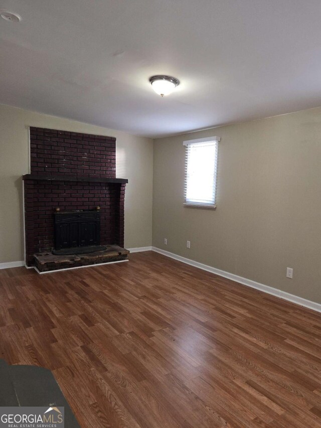 6136 Holiday Blvd, Forest Park, GA 30297 - unfurnished living room featuring a brick fireplace, wood finished floors, and baseboards