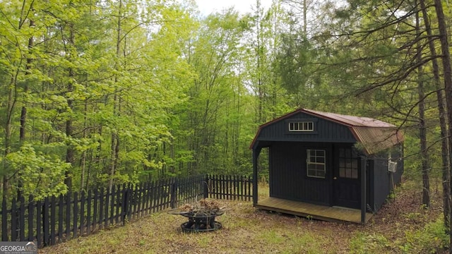 view of outdoor structure with an outbuilding, fence, a forest view, and a fire pit