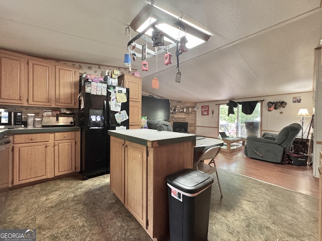 kitchen with black refrigerator with ice dispenser, open floor plan, a center island, stainless steel microwave, and a fireplace