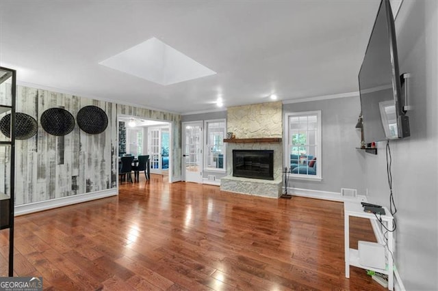 unfurnished living room with crown molding, hardwood / wood-style flooring, a stone fireplace, and baseboards