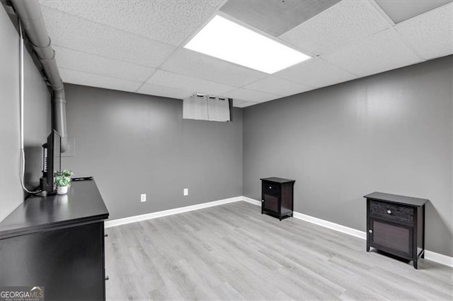 finished below grade area with light wood-type flooring, a paneled ceiling, and baseboards