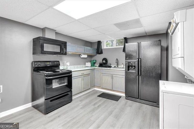 kitchen with black appliances, a sink, light wood-style floors, a drop ceiling, and light countertops