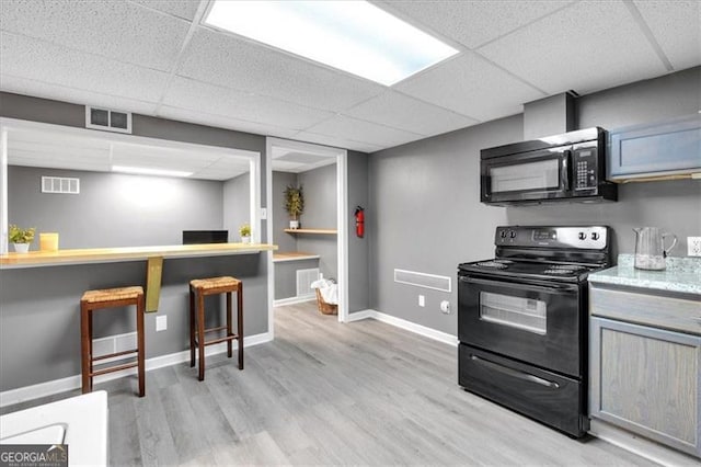 kitchen featuring black appliances, a drop ceiling, light wood-type flooring, baseboards, and light countertops