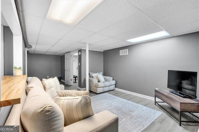 living room with wood finished floors, a drop ceiling, and baseboards